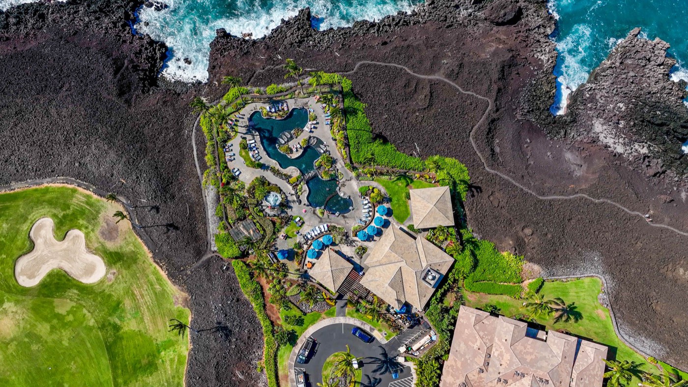Aerial view of an oceanfront Hawaiian condominium resort with lagoon pools, framed by black lava rock and the Pacific